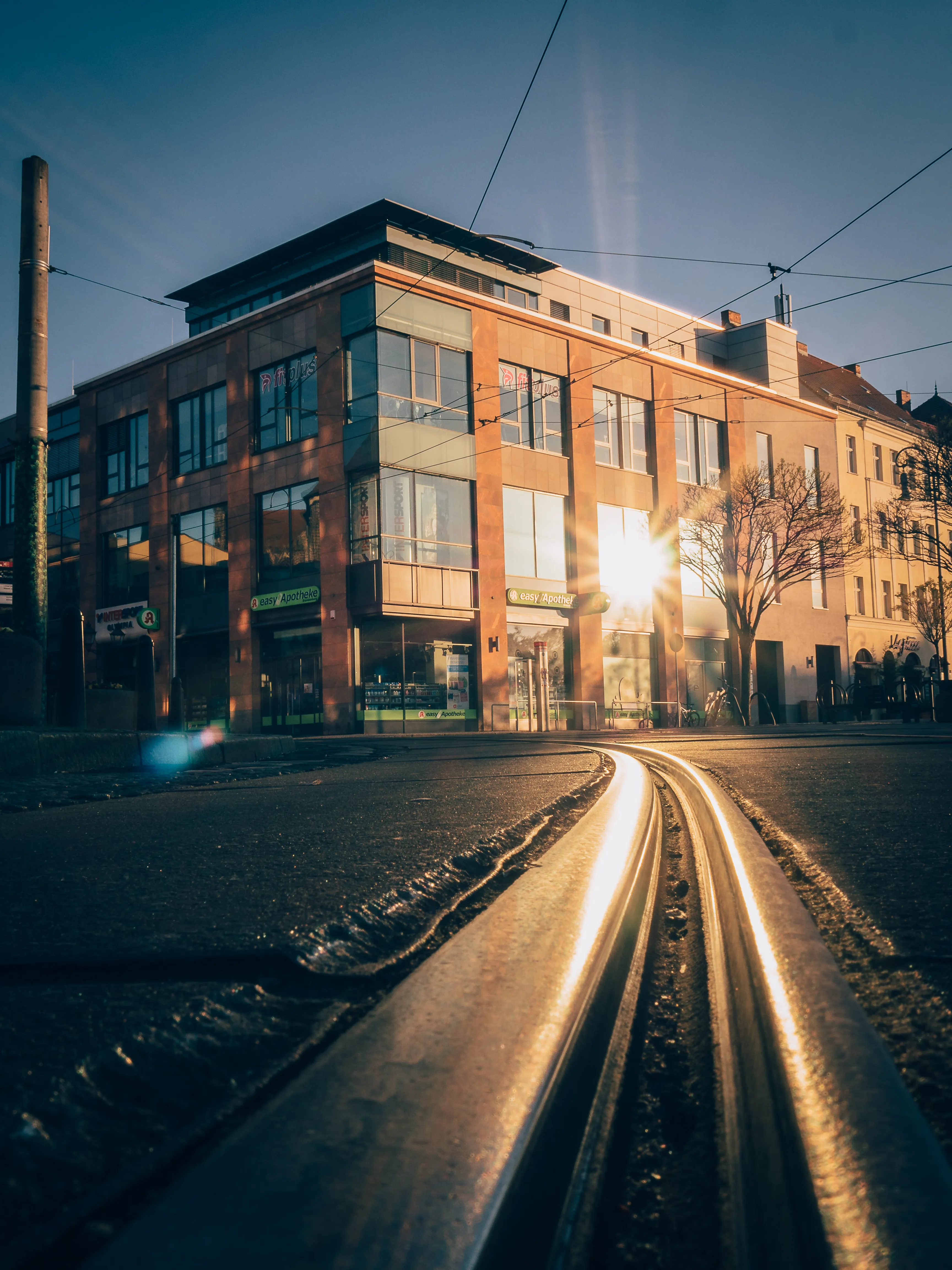 Innerstädtisches Gewerbegebäude an den Straßenbahngleisen im Gegenlicht der untergehenden Sonne — urbane Lage, klare Linien, Substanz.